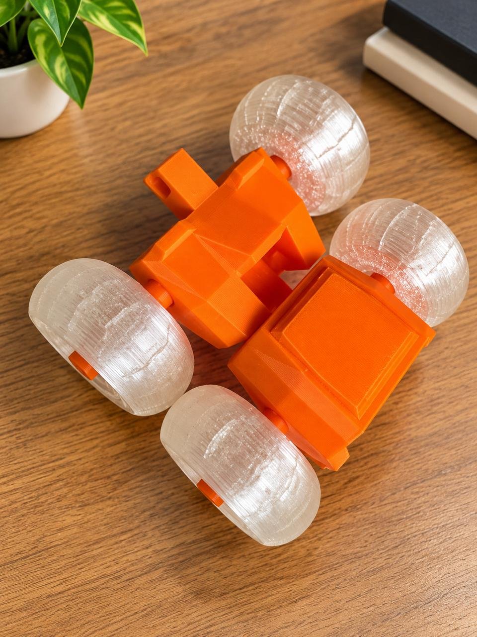Vibrant orange 3D printed stunt car featuring translucent clear wheels on a wooden workstation